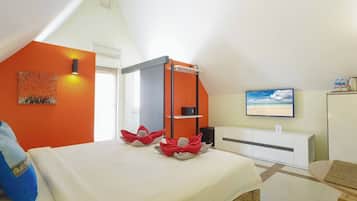 Quarto de hotel com cama, escrivaninha, televisão e janela vista para a praia.