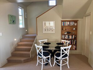 A dining area with a round table, four chairs, a staircase, a bookshelf, and a window. - Luxury beachfront villa perfectly located in Ahuriri Napier (Napier)