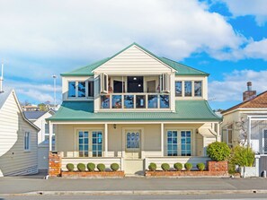 A two-story house with a green roof, a garage, and a front porch with a brick column and small trees. - Luxury beachfront villa perfectly located in Ahuriri Napier (Napier)