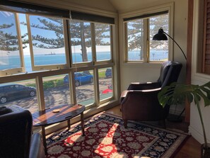 A room with a large bay window overlooking a street and a body of water, a black chair, a small table, and a patterned rug. - Luxury beachfront villa perfectly located in Ahuriri Napier (Napier)