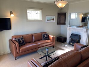 A living room with a brown leather sofa, a glass coffee table, a fireplace, and a mounted television. - Luxury beachfront villa perfectly located in Ahuriri Napier (Napier)