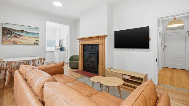 A modern living room with a leather sofa, a fireplace, a flat-screen TV, and a painting on the wall. - Sandy Bay Style | Close to CBD (Sandy Bay)
