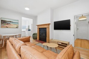 A modern living room with a leather sofa, a fireplace, a flat-screen TV, and a painting on the wall. - Sandy Bay Style | Close to CBD (Sandy Bay)