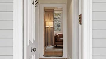 A hallway with a wooden floor, a lamp, a brown leather chair, and a window with curtains.