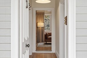 A hallway with a wooden floor, a lamp, a brown leather chair, and a window with curtains. - Sandy Bay Style | Close to CBD (Sandy Bay)