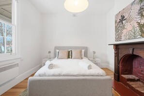 A bedroom with a bed, bedside tables, a fireplace, and a window. - Sandy Bay Style | Close to CBD (Sandy Bay)
