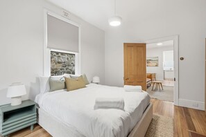 A bedroom with a bed, bedside tables, a stone wall, a wooden door, and a view of another room. - Sandy Bay Style | Close to CBD (Sandy Bay)