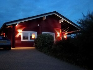 Eine rote Holzhütte mit befestigter Auffahrt und einem geparkten Auto davor.