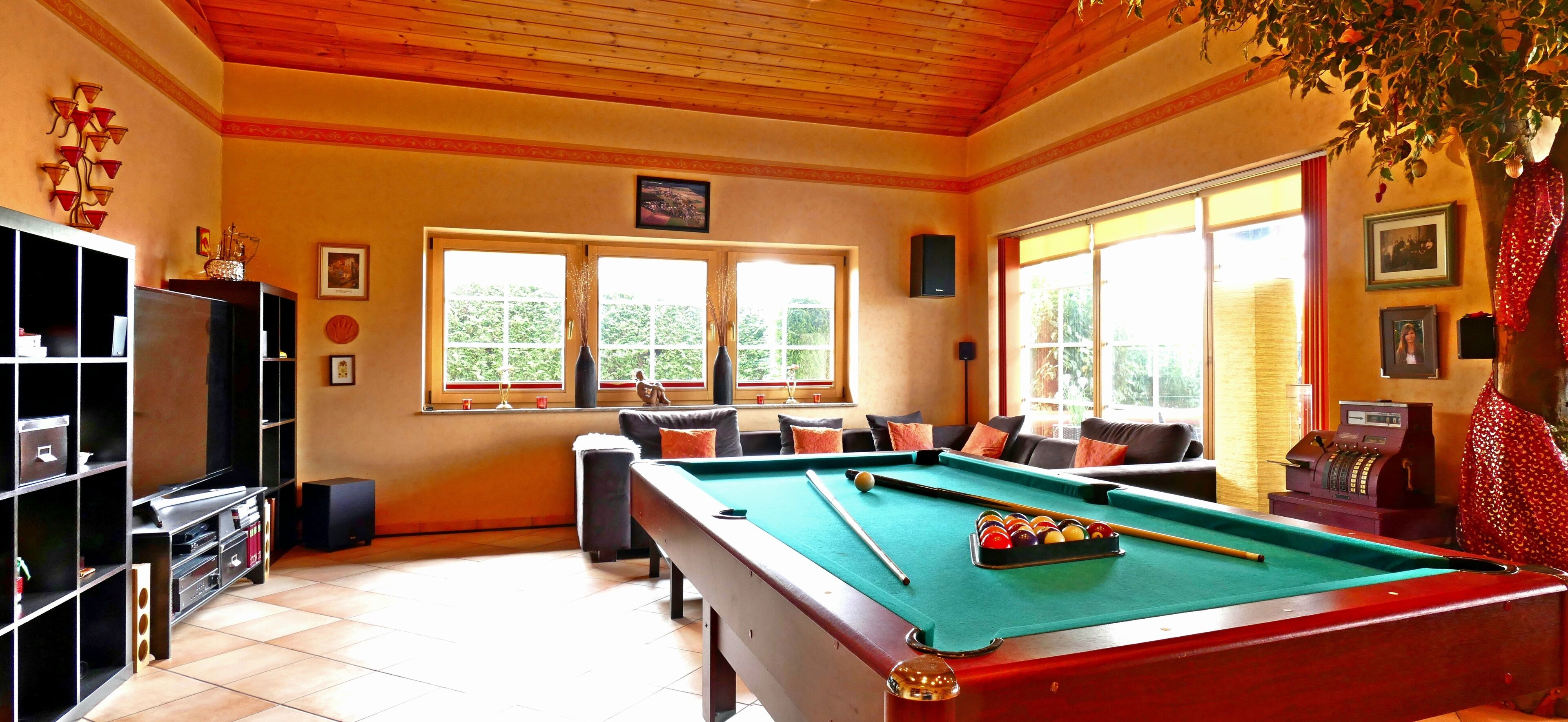 Une table de billard dans une pièce dotée d’un plafond en bois, d’un canapé avec des coussins et d’une bibliothèque.