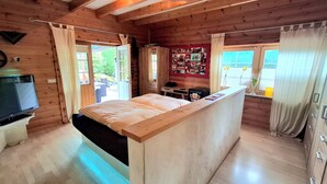 A wooden cabin room with a bed, a desk, a TV, and a window with curtains. - Pool Lodge Westerwald - Stylish Accommodations and Relaxation (Steimel-Weroth)
