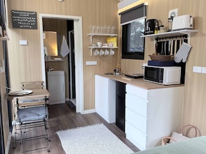 A compact kitchen with a microwave, kettle, and coffee maker on the counter, a small sink, and a window above the counter.