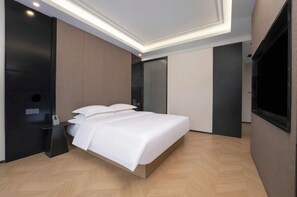 A modern hotel room with a large bed, a bedside table, a flat-screen TV, and a built-in wardrobe.