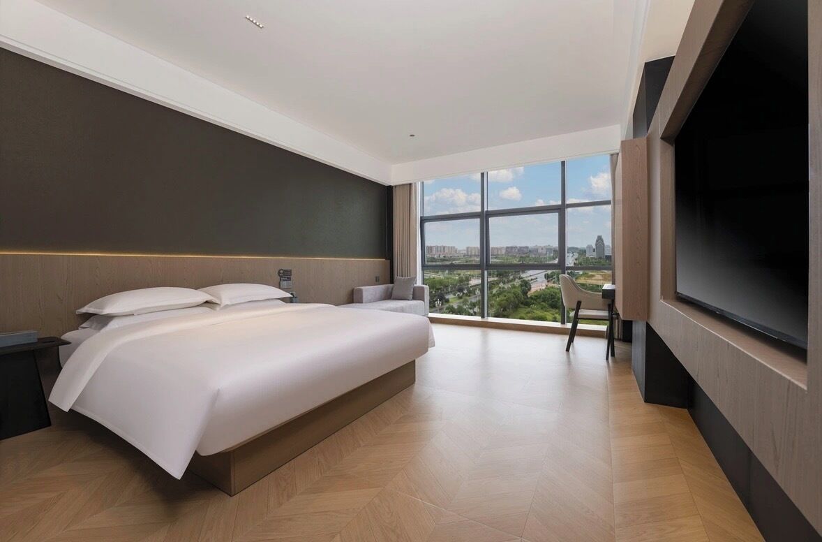 A modern hotel room with a large bed, a TV, and a city view.