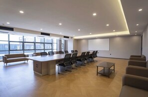 Un salón de conferencias con una larga mesa, sillas, un sofá y una pantalla para proyector.