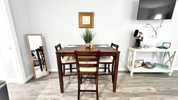 A dining area with a wooden table, four chairs, a small plant, a framed picture, and a television mounted on the wall.