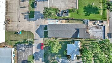 An aerial view of a parking lot with multiple vehicles, a building with a sloped roof, and surrounding greenery.