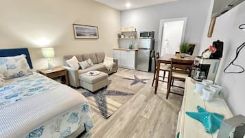 A compact hotel room with a bed, a sofa, a small kitchenette, and a dining area.