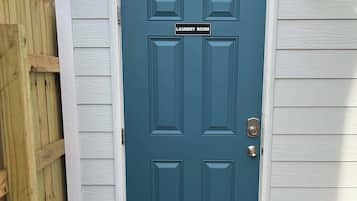A dark blue door with a sign indicating a laundry room, a wooden fence to the left, and a light-colored exterior wall.