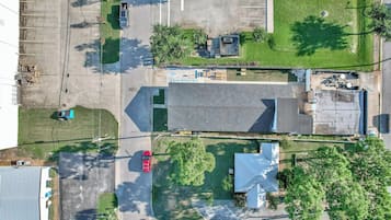An aerial view of a parking lot with multiple vehicles, a building with a sloped roof, and surrounding greenery.