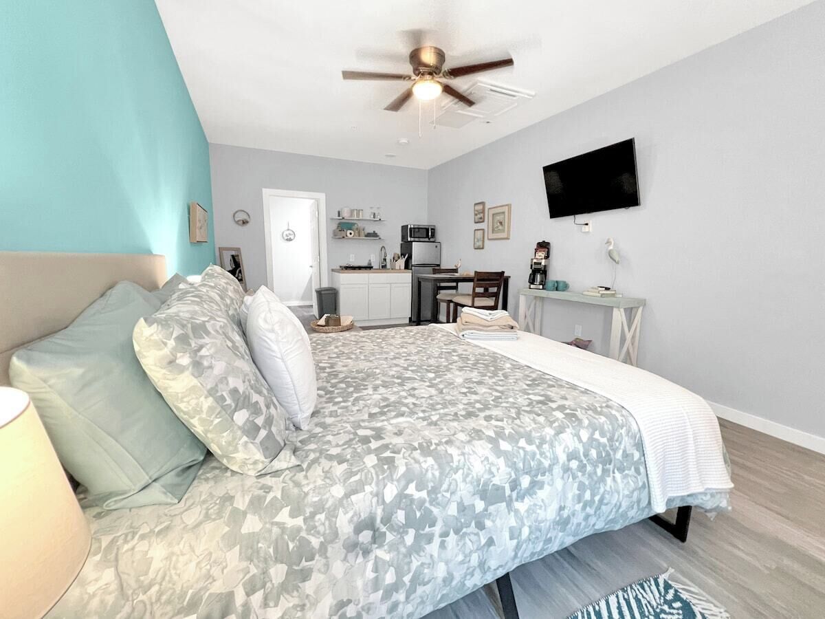 A bedroom with a bed, a ceiling fan, a TV, a kitchenette, and a bathroom.