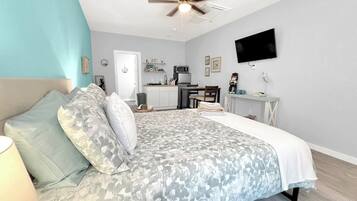 A bedroom with a bed, a ceiling fan, a TV, a kitchenette, and a bathroom.