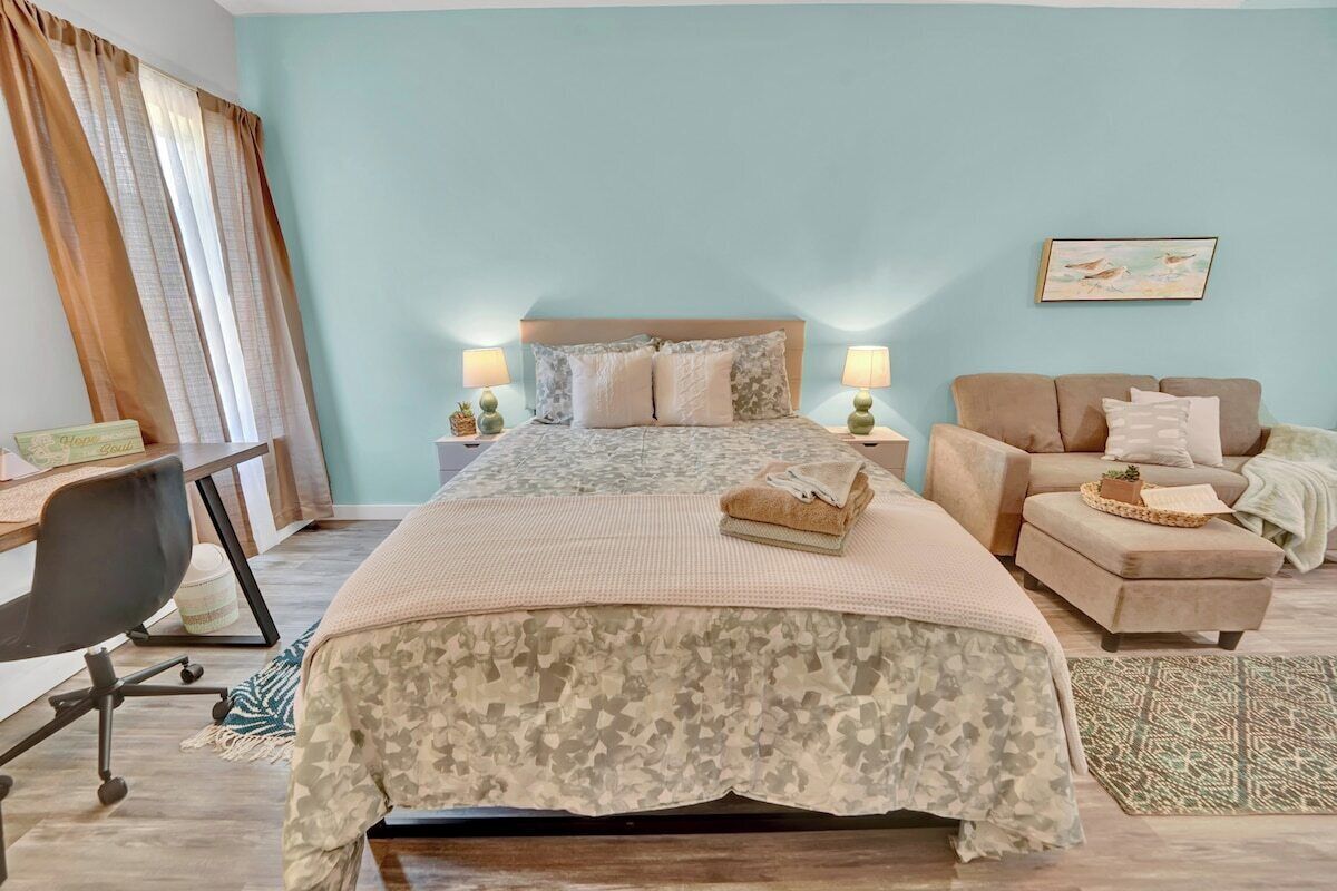 A bedroom with a bed, bedside tables, a desk, a chair, a sofa, and a rug.