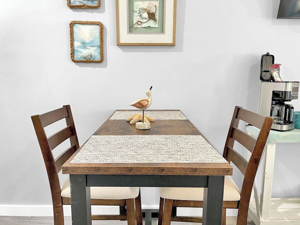 A dining table with a woven placemat, two wooden chairs, and a bird sculpture centerpiece.