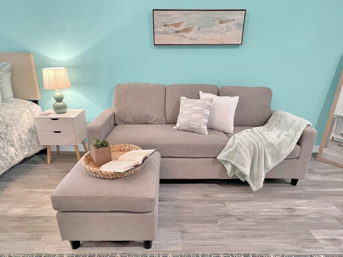 A bedroom with a bed, a nightstand, a lamp, a sofa, and a painting on the wall.