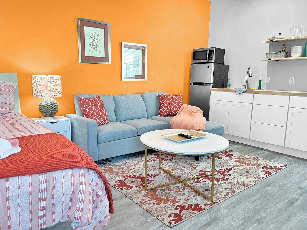 A modern living room with a sofa, a coffee table, and a bed with a patterned bedspread.