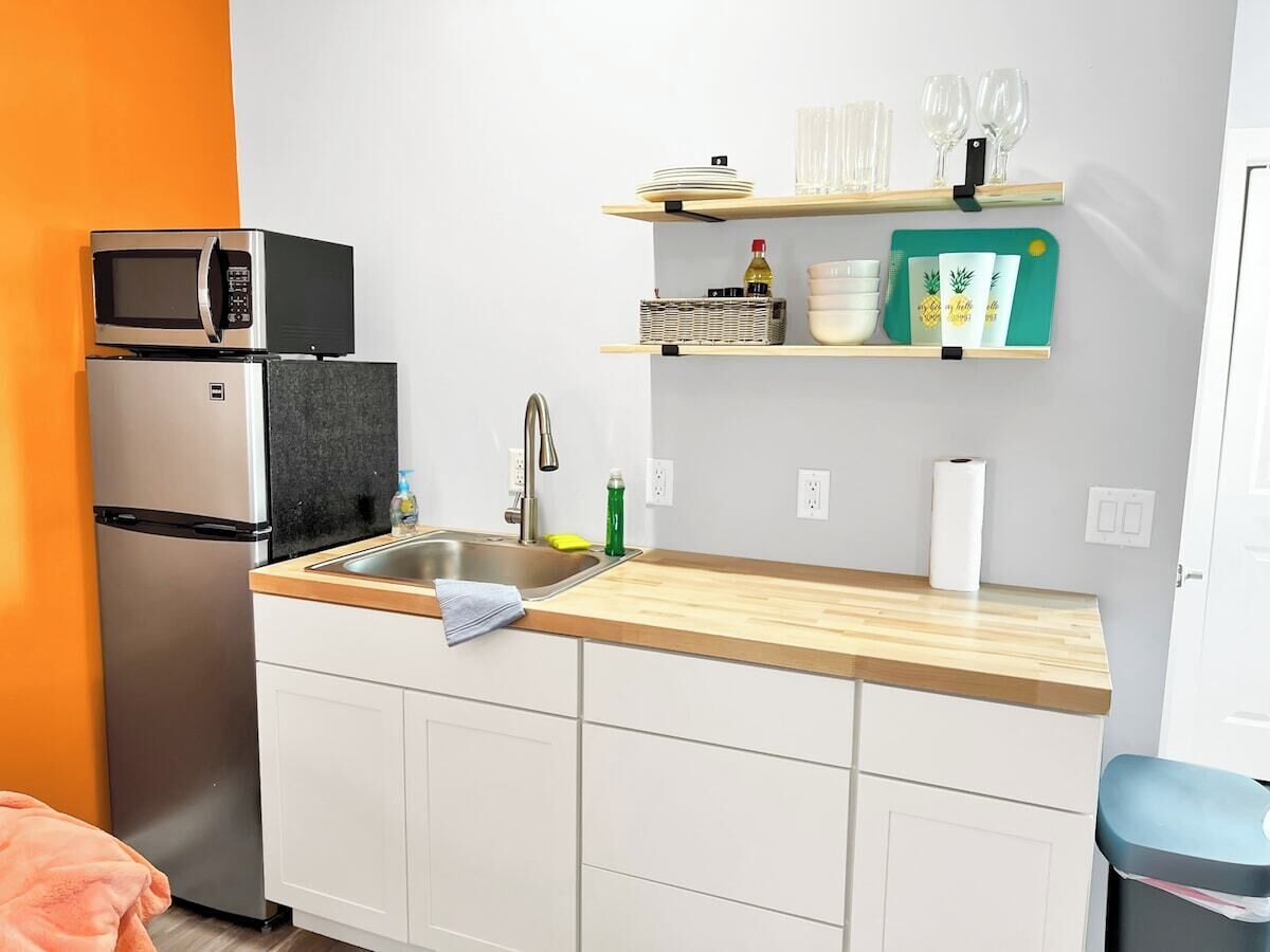A compact kitchen with a refrigerator, microwave, sink, and wooden countertop.