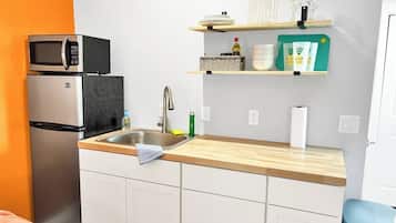 A compact kitchen with a refrigerator, microwave, sink, and wooden countertop.