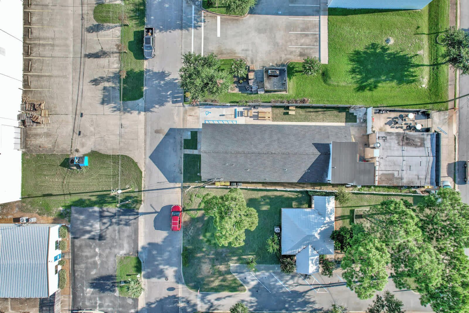 Ilmakuva parkkipaikasta, jossa on useita ajoneuvoja, loivarinteinen katto omaava rakennus ja ympäröivää viheraluetta.
