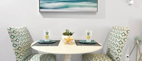A dining area with a round table, two patterned chairs, a starfish decoration, and a wall-mounted TV.