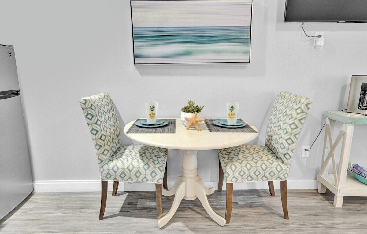 A dining area with a round table, two patterned chairs, a starfish decoration, and a painting of a seascape on the wall.
