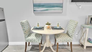 A dining area with a round table, two patterned chairs, a starfish decoration, and a painting of a seascape on the wall.