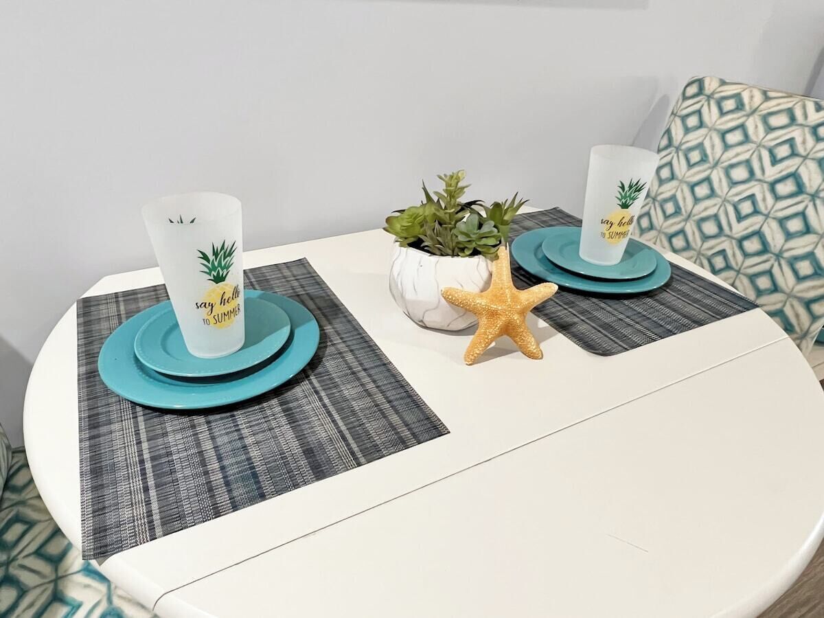 Una mesa redonda con dos vasos blancos sobre posavasos color aguamarina, una pequeña planta en maceta y una decoración con una estrella de mar.