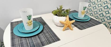 Una mesa redonda con dos vasos blancos sobre posavasos color aguamarina, una pequeña planta en maceta y una decoración con una estrella de mar.