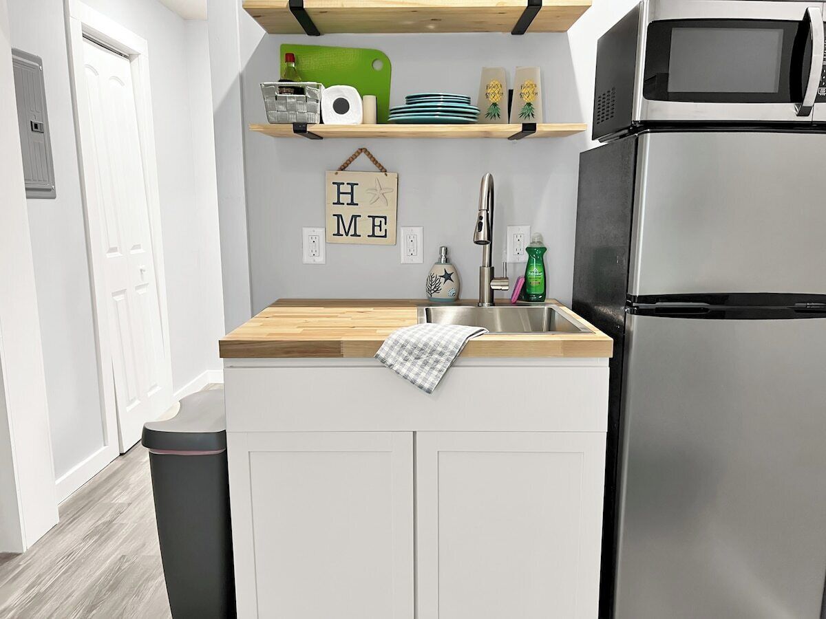 A kitchen with a stainless steel refrigerator, a wooden countertop, a sink, and a 'HOME' sign on the wall.