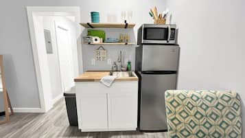 A compact kitchen with a built-in microwave, a refrigerator, and a wooden countertop.