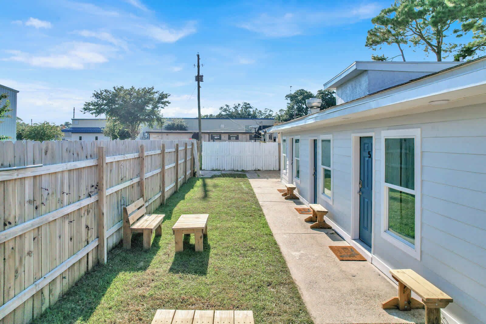 A fenced backyard with a grassy area, wooden benches, and a building with windows.