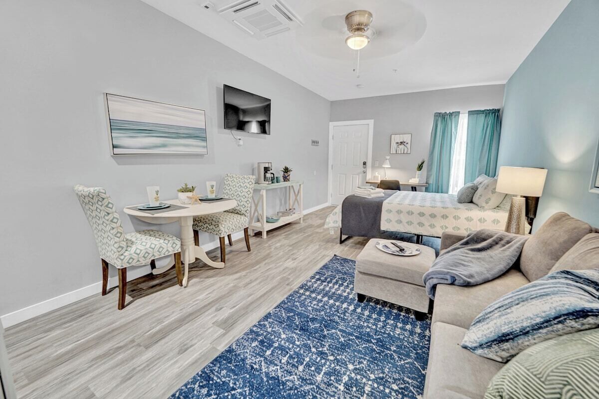 A modern living room with a sofa, a coffee table, a dining area with chairs, and a television mounted on the wall.