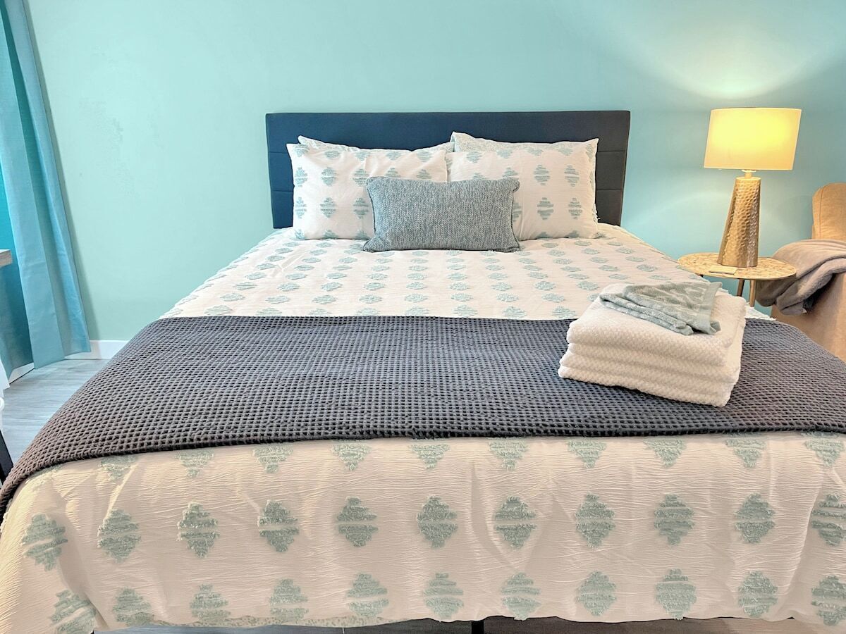 A neatly made bed with a patterned bedspread, pillows, and a folded towel.