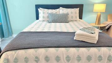 A neatly made bed with a patterned bedspread, pillows, and a folded towel.