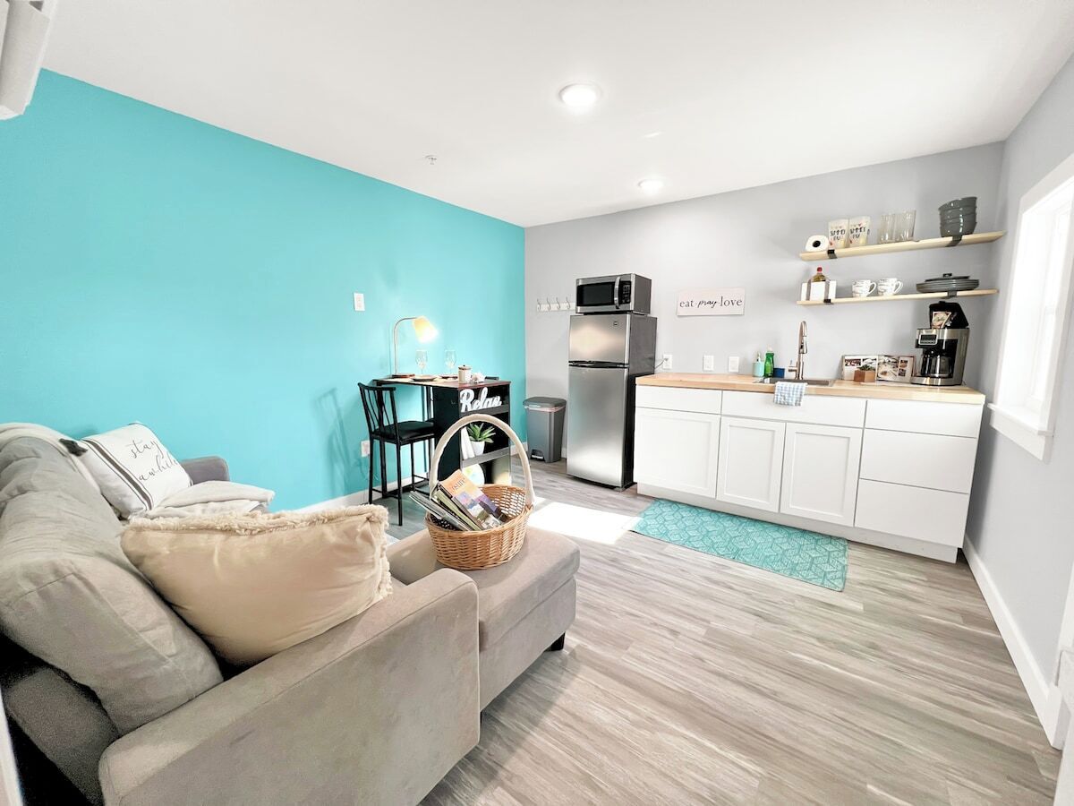 A compact living space with a kitchenette, a sofa, a dining table, and a teal accent wall.