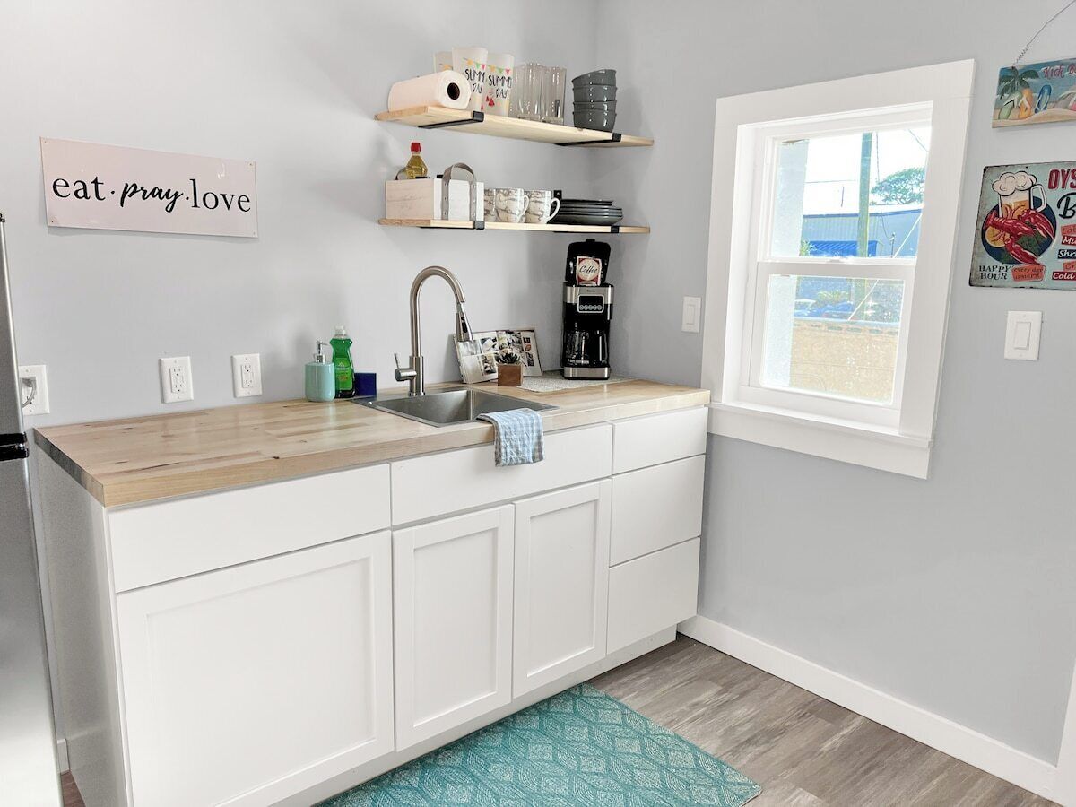 A kitchen with white cabinets, a wooden countertop, a coffee maker, and a window with a view.