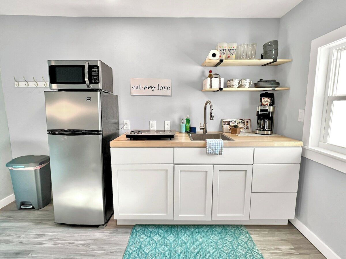 A compact kitchen with a stainless steel refrigerator, a microwave, a coffee maker, and a sink.