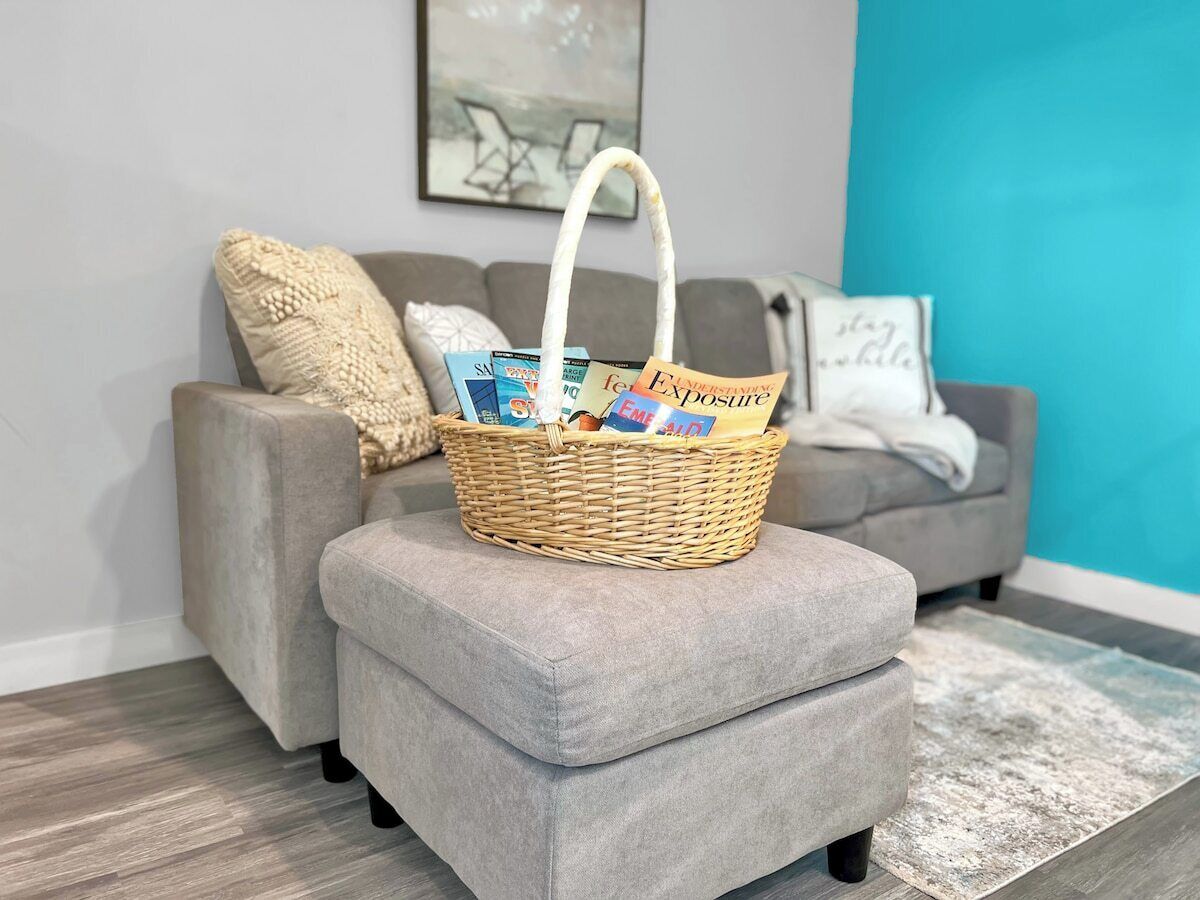 A grey sofa with a woven basket on top, a grey ottoman, and a blue accent wall.