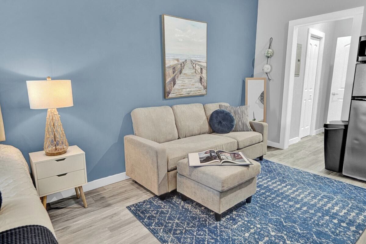 A living room with a sofa, ottoman, and a lamp on a nightstand.