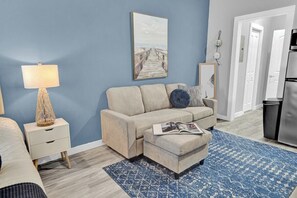 Ein Wohnzimmer mit Sofa, Hocker und einer Lampe auf einem Nachttisch.