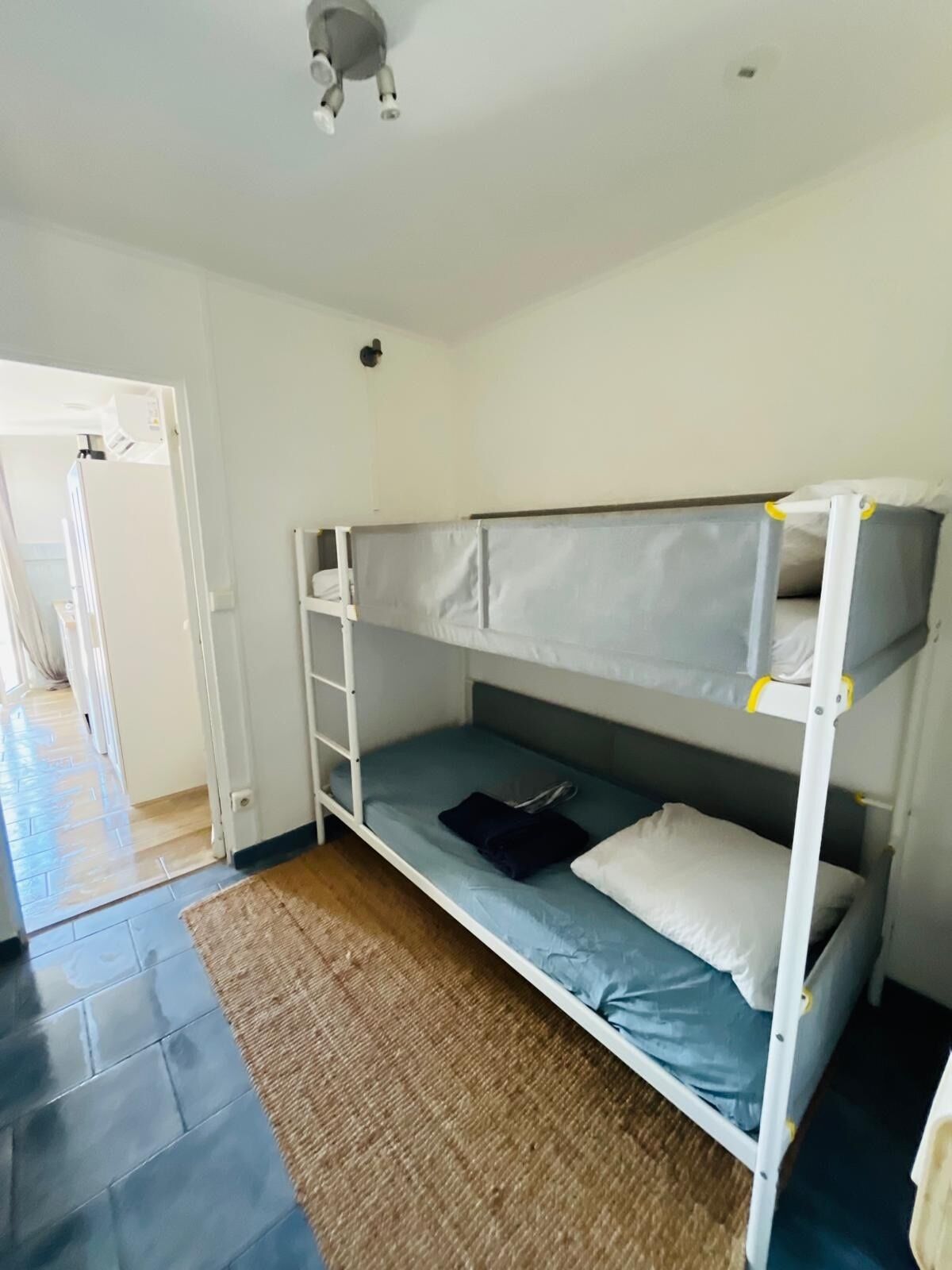 A bunk bed room with a white ladder, a blue mattress, and a brown rug.